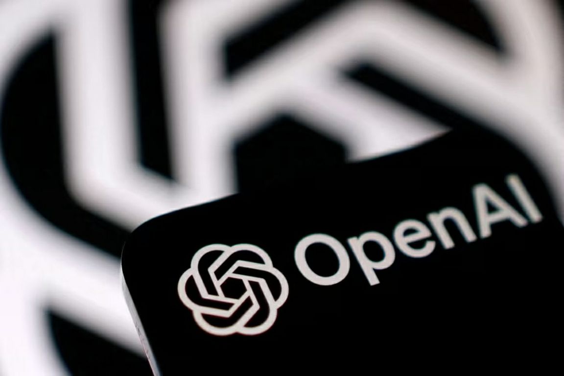 The OpenAI logo appears on a smartphone in front of an enlarged version of the company’s logo.