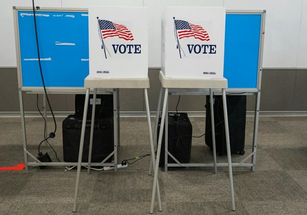 Two voting booths featuring American flags and the word “VOTE” stand in front of privacy screens at a polling place.
