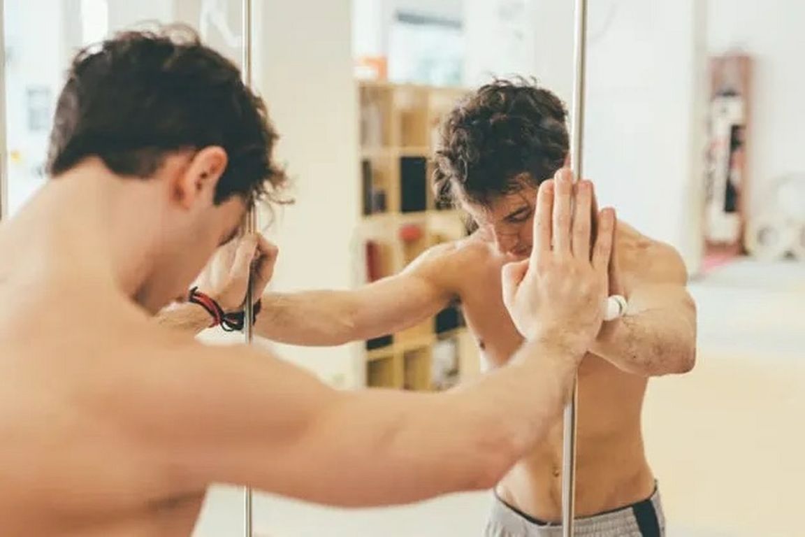 A shirtless man examines his reflection in a mirror, illustrating the social media trend known as “looksmaxxing.”
