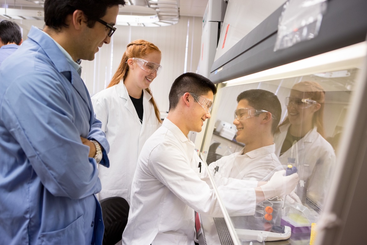 Three UCLA researchers wearing protective eyewear work together at a laboratory workstation, with one conducting an experiment as the others observe.