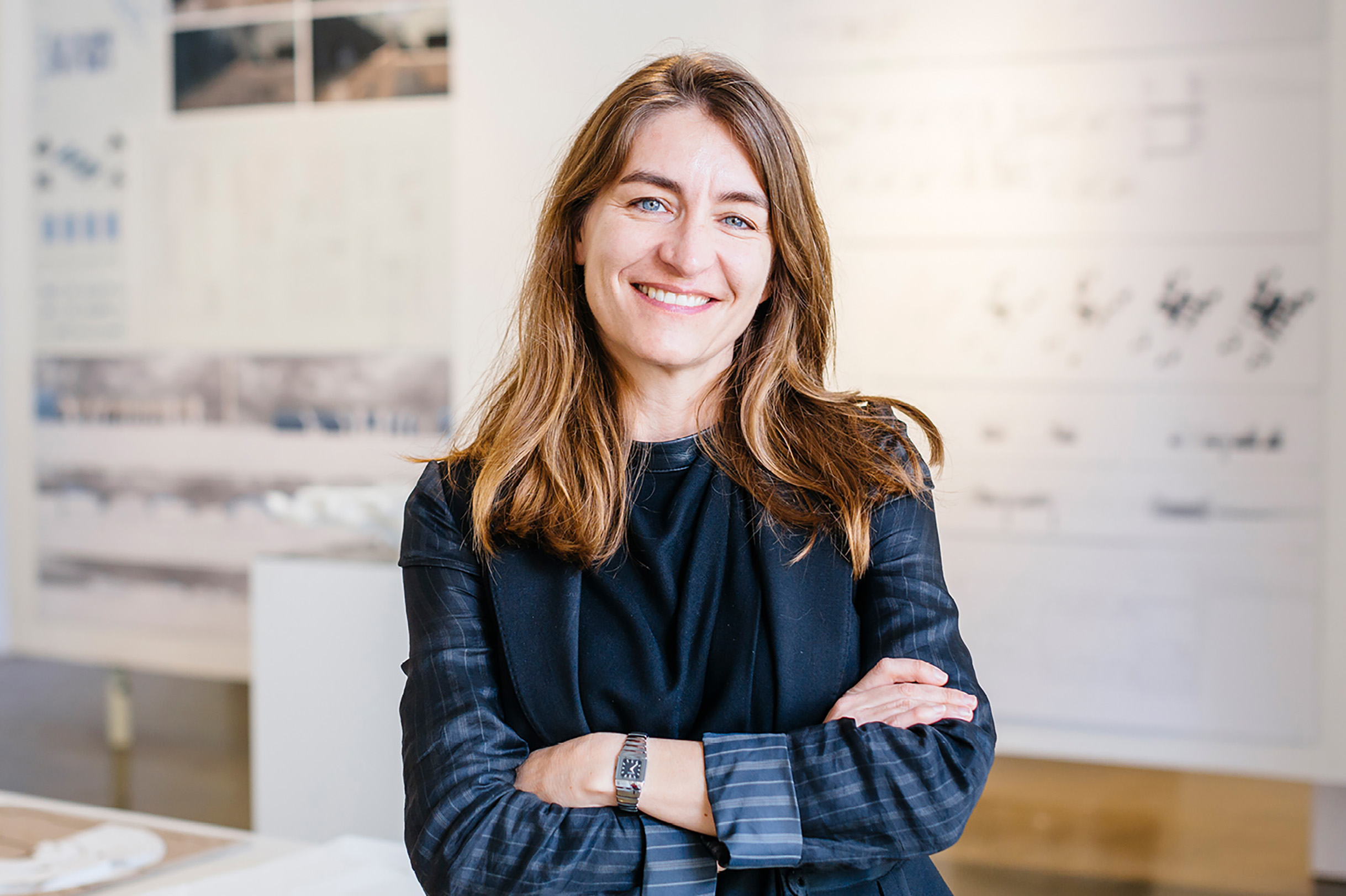 Heather Roberge, standing with her arms crossed in a bright office while wearing a dark blue top and patterned jacket.