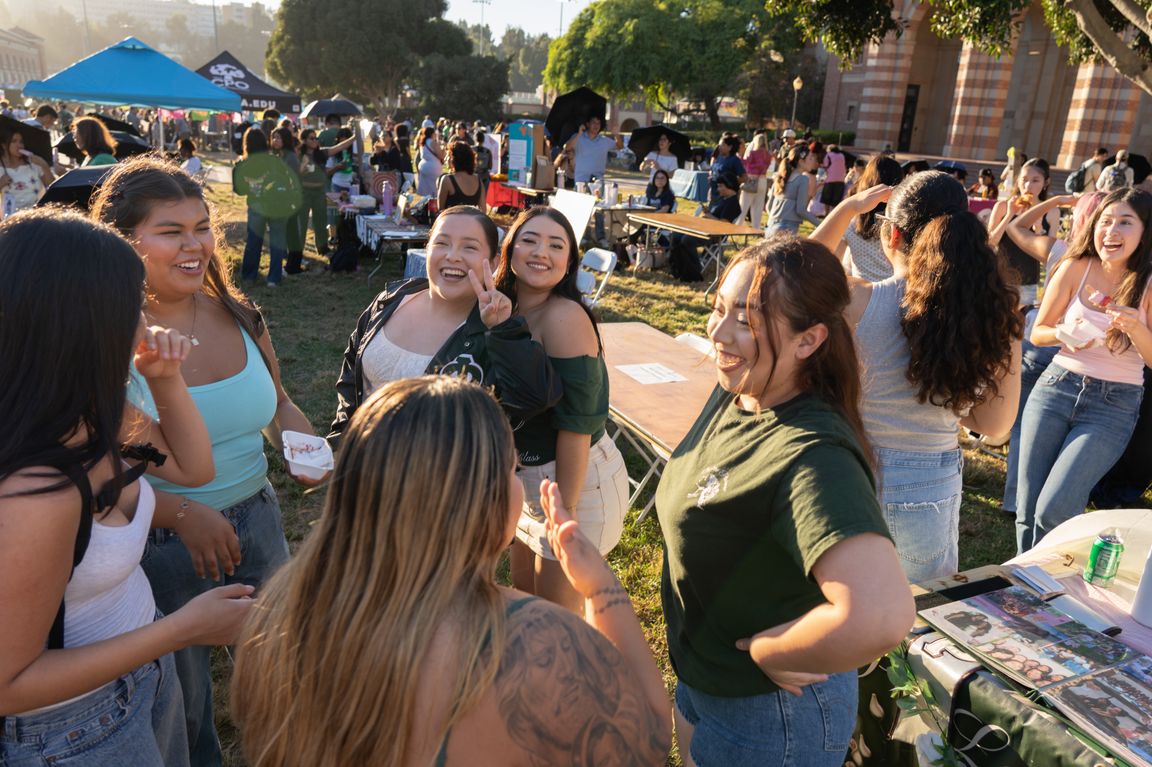 Students smile, laugh and mingle on a sunlit lawn during UCLA’s 2026 Latinx Welcome celebration, with tables, event tents and other attendees gathered in the background.