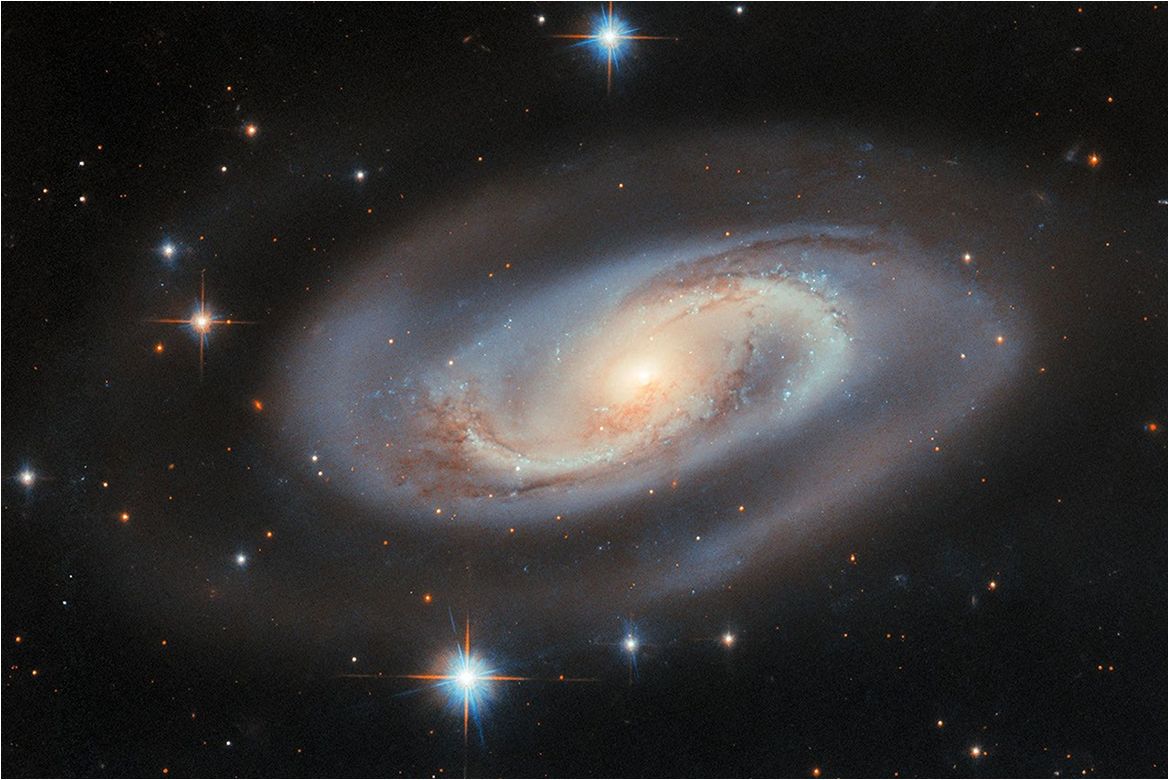 A glowing spiral galaxy with a bright yellow-white core, blue outer arms and dark dust lanes surrounded by stars against a black background.
