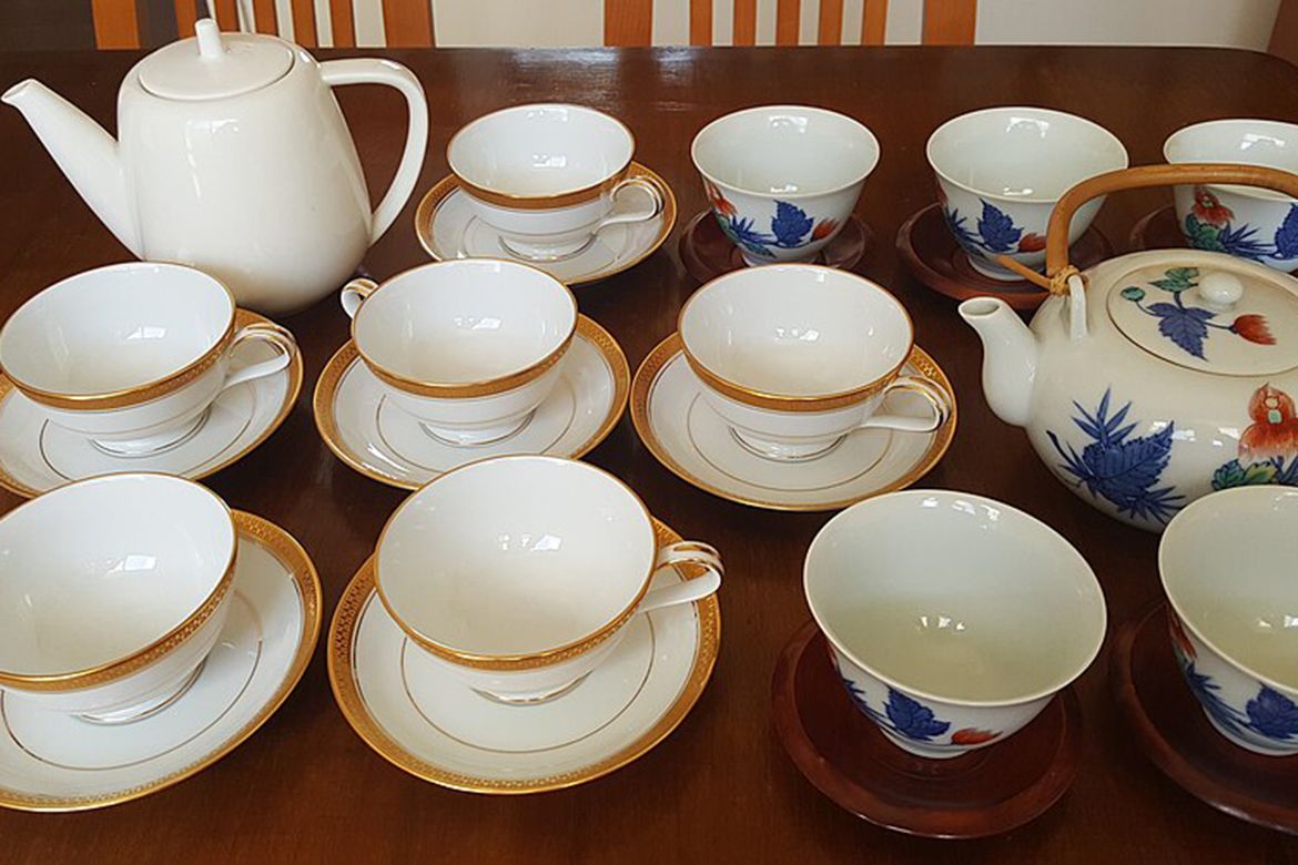 Two white teapots with matching cups and saucers lined up on a brown table.