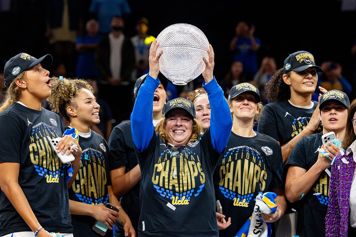UCLA women's basketball team after winning the championship. The team is cheering, with someone in the middle holding up a trophy.