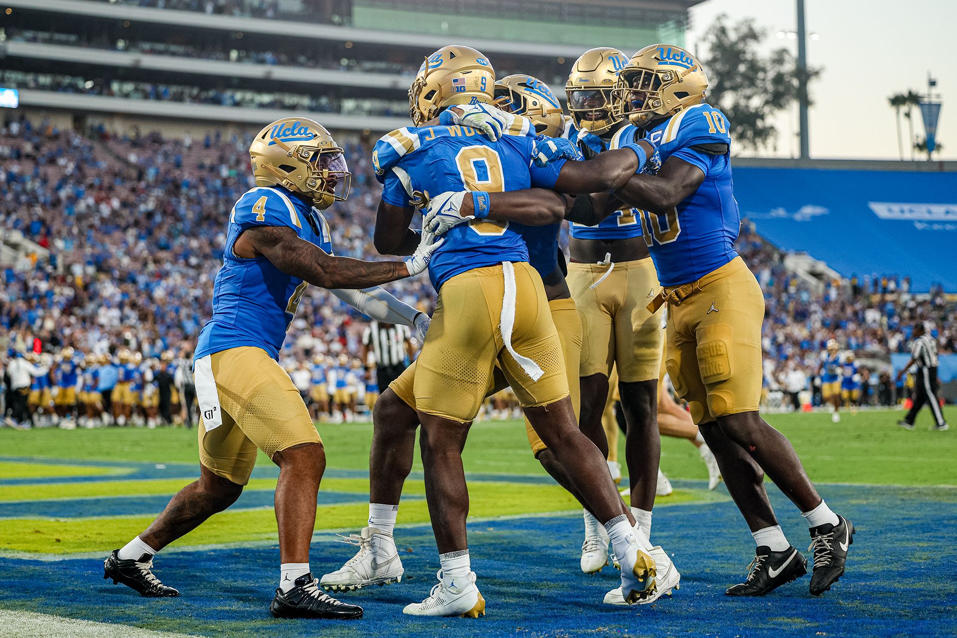 UCLA Football team huddled together, jumping and cheering on a football field.