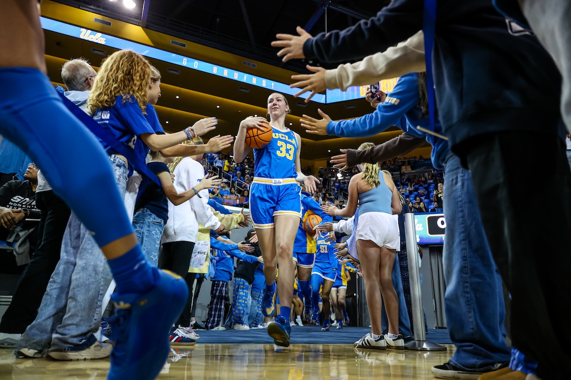 UCLA center Amanda Muse carries a basketball onto the court as fans reach out to greet her.