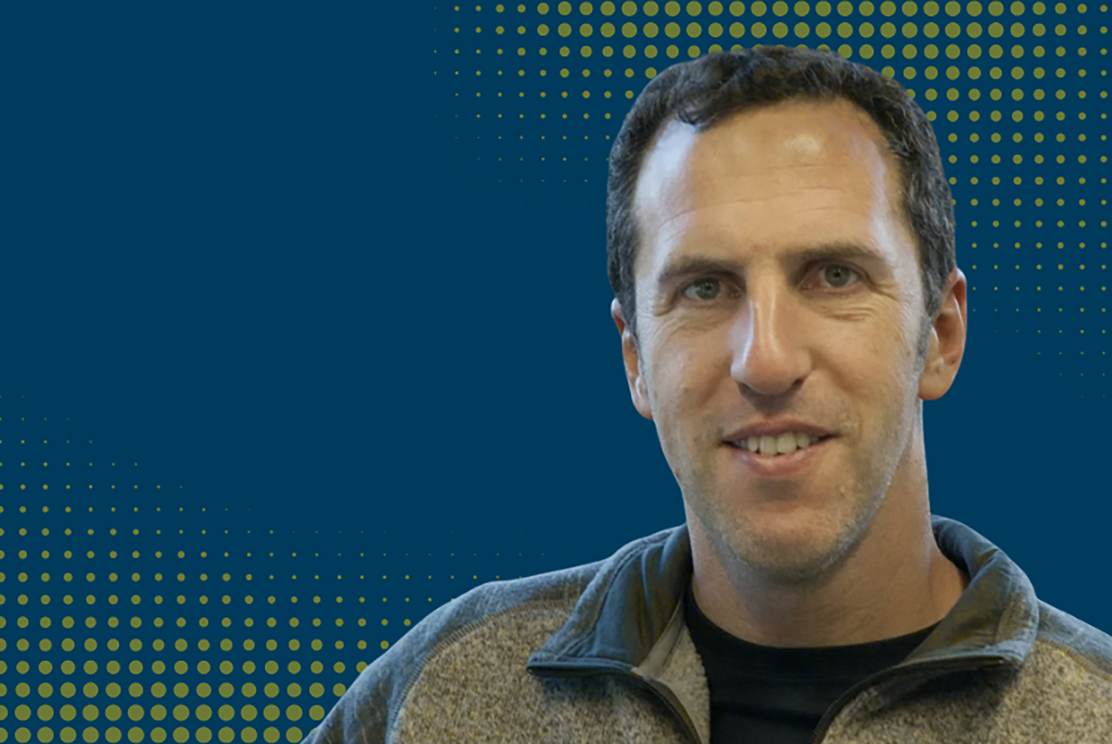 Ariel Burstein wearing a gray fleece jacket against a dark teal background with a decorative yellow dotted pattern.