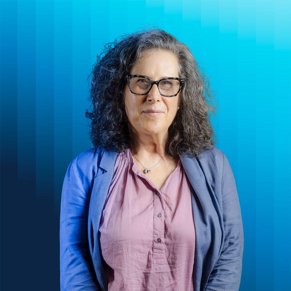 Portrait of Helen Deutsch in mauve top and blue jacket against blue background.