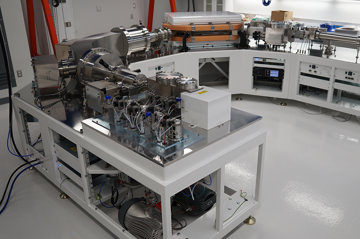 Large scientific instrument with stainless-steel components, tubing, wiring, control panels and pumps arranged on a laboratory workbench.
