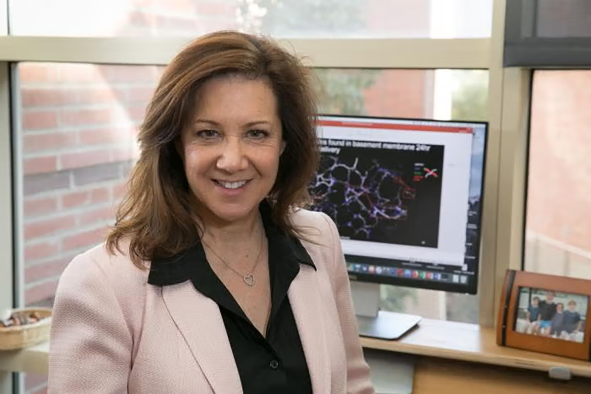 Melissa Spencer, wearing a light pink blazer and black blouse, in an office beside a computer displaying scientific research.
