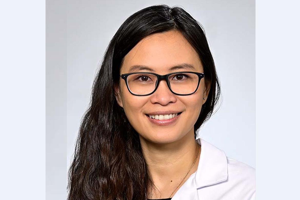 Headshot of Tue Te wearing white coat and glasses against a light gray background.