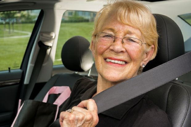 Smiling senior mature driver holding seatbelt