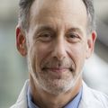 Jeffrey Kaye, M.D., has short gray straight hair, and a light blue collared shirt under a medical white coat.