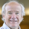 Deloughery has short gray/white hair, a gray shirt, smiling.