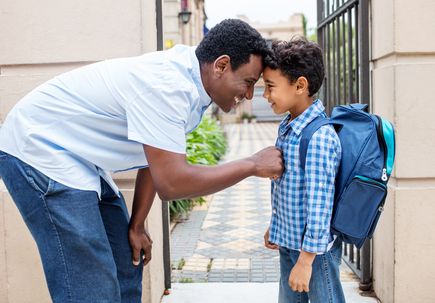 Smiling father leaving son with backpack to school