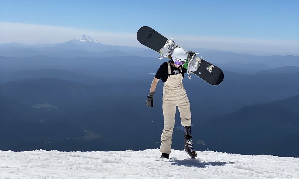 Rebecca Johnston in snow gear atop a snowy mountain, preparing to snowboard. After recovering from osteosarcoma, Rebecca Johnston made the decision to amputate her left leg above the knee. Since then, she has become a World Cup parasnowboarder who has competed around the world for Team USA. She’s now training for the 2026 Winter Paralympics in Milan, Italy.&nbsp;(Photo courtesy of Rebecca Johnston)