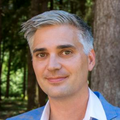 Jonah Sacha, Ph.D., has a light blue shirt on, blue blazer, and gray hair, smiling in a green area of OHSU.
