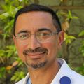 Ashok Muralidaran, M.D., has short black hair, eye glasses and wearing a white coat in the garden at Doernbecher Children's Hospital.