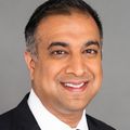 Aadam Hussain (OHSU) is wearing a black suit, white shirt, and black tie. Hussain is smiling and has gray/black hair.