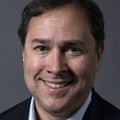 John Hershey (OHSU) wearing a black jacket and blue button shirt, smiling, with dark brown hair.