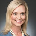 Kelly Schrader (OHSU) has light blonde hair, she is smiling, and is wearing a blue top and pearl necklace.
