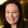 Carolyn Schutt Ibsen, Ph.D., has long dark hair, a black jacket and green top, smiling in a dimly lit area.