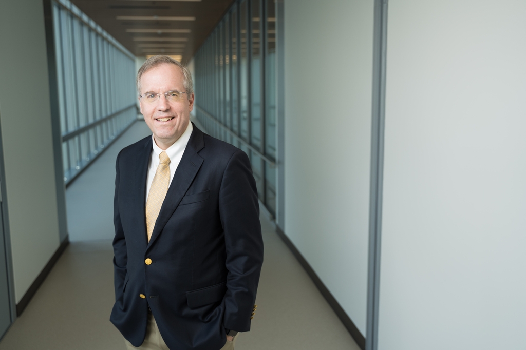 Nathan Selden, M.D., Ph.D., has short gray hair, glasses, a dark suit and smiling in a hallway at OHSU.