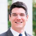 Tyler Tate, M.D., has short dark hair, wearing a suit and tie, standing near the BICC library.