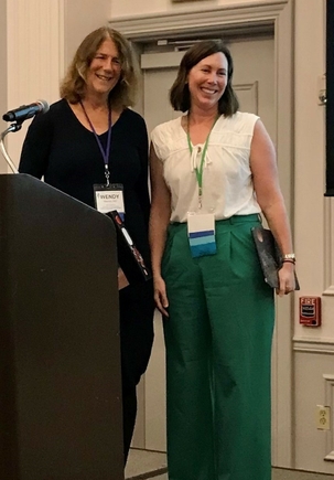 Wendy Warren, M.D., left, and Nellie Wirsing, M.D., both with shoulder-length brown hair, standing at a podium.