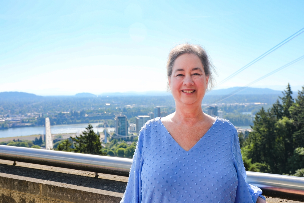 Kathy Hart, wearing a blue shirt and short hair pulled back, standing on a terrace at OHSU. Kathy Hart is on the path to recovery following a rare skin and musculature condition that ultimately revealed stage 3 uterine cancer. She has a good prognosis with the benefit of complex, multidisciplinary care at OHSU. (OHSU/Christine Torres Hicks)