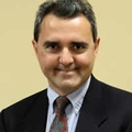 Kirk Lalwani, M.D., has short gray, black hair, wearing a suit and red tie, smiling.