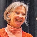 Jackie Shannon, Ph.D., tiene el pelo corto y gris, un suéter naranja y pantalones marrones, y so