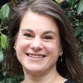 Rebecca Jungbauer, Dra. PH., M.A., tiene cabello castaño hasta los hombros y una blusa azul, y sonríe en un jardín cerca del Hospital Infantil Doernbecher.