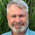 Gary Nesbit, M.D., has short white hair and facial hair, smiling, wearing an aqua shirt.