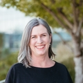 Laurie King, Ph.D., PT, MCR, has shoulder-length gray/blonde hair, a dark top and smiling on a balcony at OHSU.