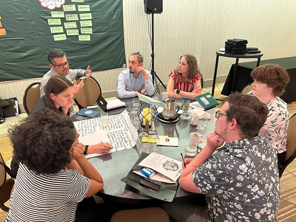 Varias personas alrededor de una mesa conversando y colaborando en planes de extensión comunitaria.