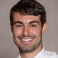 Chris Eden M.D. has short dark hair and is smining while wearing a white coat.