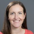 Brigit Hatch, M.D. (OHSU) is wearing an orange shirt, has long brown hair and is smiling.
