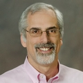 John Kaufman, M.D., M.S. (OHSU), in a dress shirt and glasses, smiling.