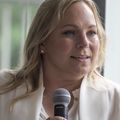 Joni Busche, que tiene cabello rubio hasta los hombros y viste una camisa blanca con un suéter blanco, se sienta en la reunión del panel de información sobre fentanilo en OHSU.