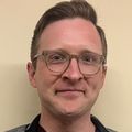 Ben Khalil, M.D., has short dark blond hair, eye glasses, and smiling against a beige background.
