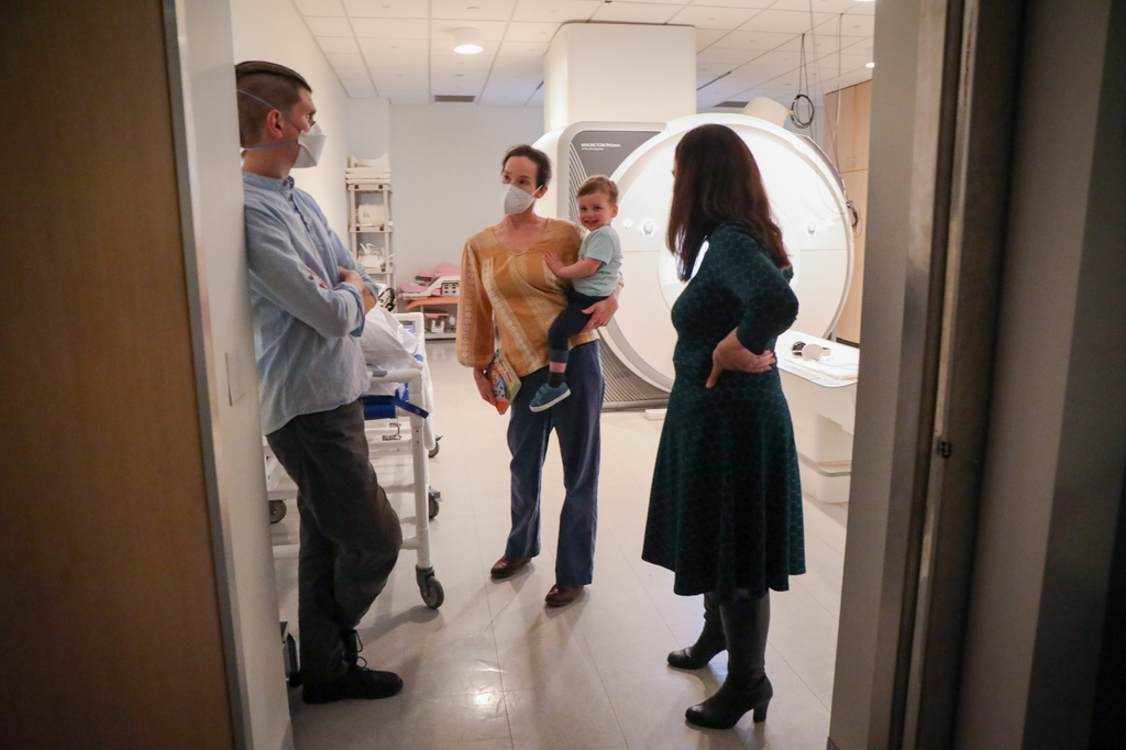 Tres adultos hablando en una sala de resonancia magnética, un adulto sosteniendo a un niño pequeño. Investigadores/as del Center for Mental Health Innovation de OHSU identificaron nuevos biomarcadores relacionados con la composición de grasa corporal durante el embarazo que se relacionan con resultados de salud mental en los hijos/as. (OHSU/Christine Torres Hicks)
