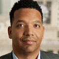 Damien Hall has short black hair, a gray suit and smiling in an office room.