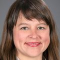Lori K. Howell, M.D., FAAP, tiene cabello largo y castaño con flequillo lateral, una blusa blanca y una chaqueta negra, y sonríe sobre un fondo gris.