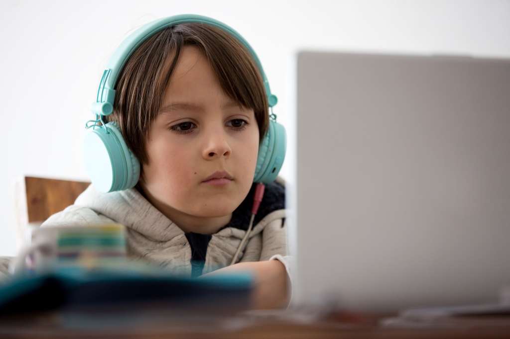 Un niño con auriculares en las orejas mientras mira la pantalla de una computadora. Un estudio de OHSU halló que el ruido blanco y el ruido rosa brindan un beneficio pequeño pero significativo para niños y adultos de edad universitaria con TDAH o síntomas de TDAH. (Getty Images)