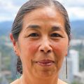 Lynne Shinto, N.D., M.P.H., tiene el pelo largo y oscuro, recogido en una coleta baja. Ella está parada en un balcón de OHSU con vista a la ciudad de Portland.