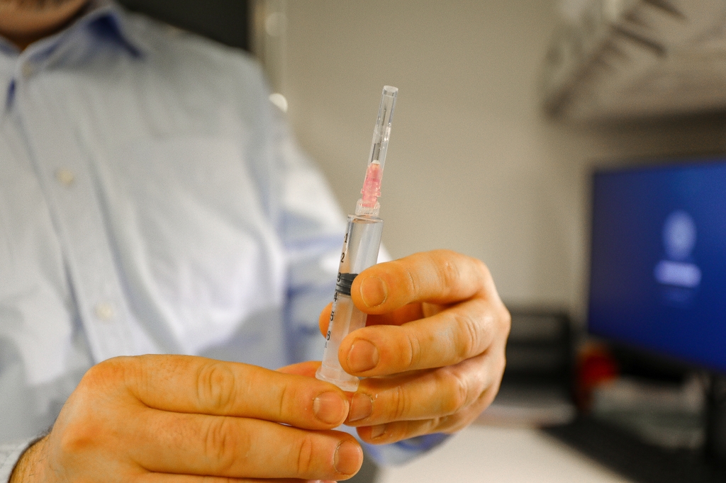 Una persona sostiene una jeringa con una vacuna en un laboratorio. Un estudio en primates no humanos encontró una disminución dramática en los niveles de la forma de VIH en monos después de una inyección de Partículas Interferentes Terapéuticas, o TIP. Los resultados del estudio sugieren que una inyección de TIP podría evitar que una persona que vive con el VIH transmita el virus a otra persona. Los resultados de esta investigación se utilizarán para informar un ensayo clínico planificado en personas. (OHSU/Christine Torres Hicks)