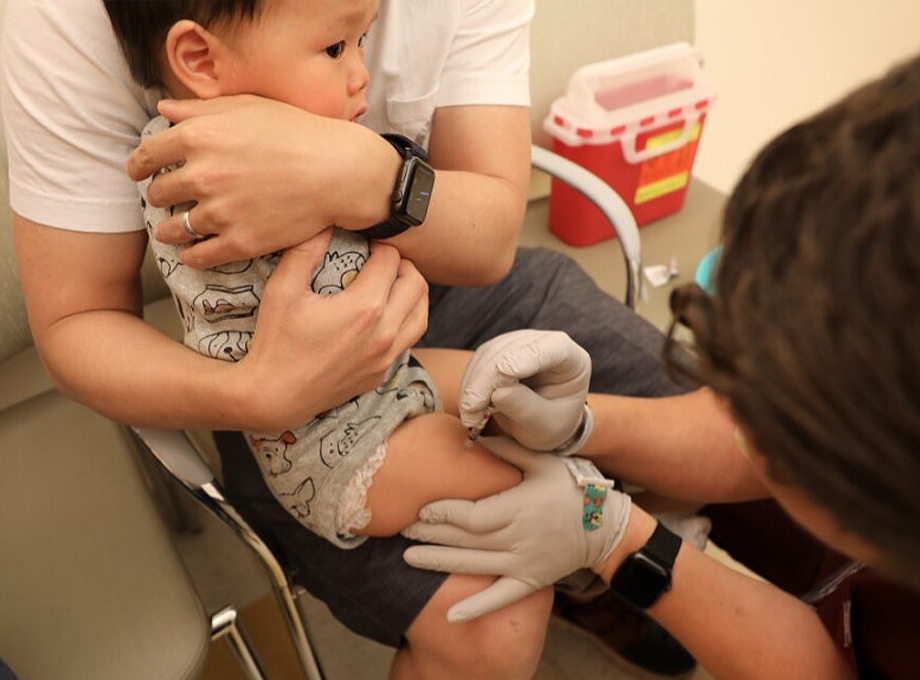 Un niño se sienta sobre uno de sus padres esperando la inyección de la vacuna en OHSU.