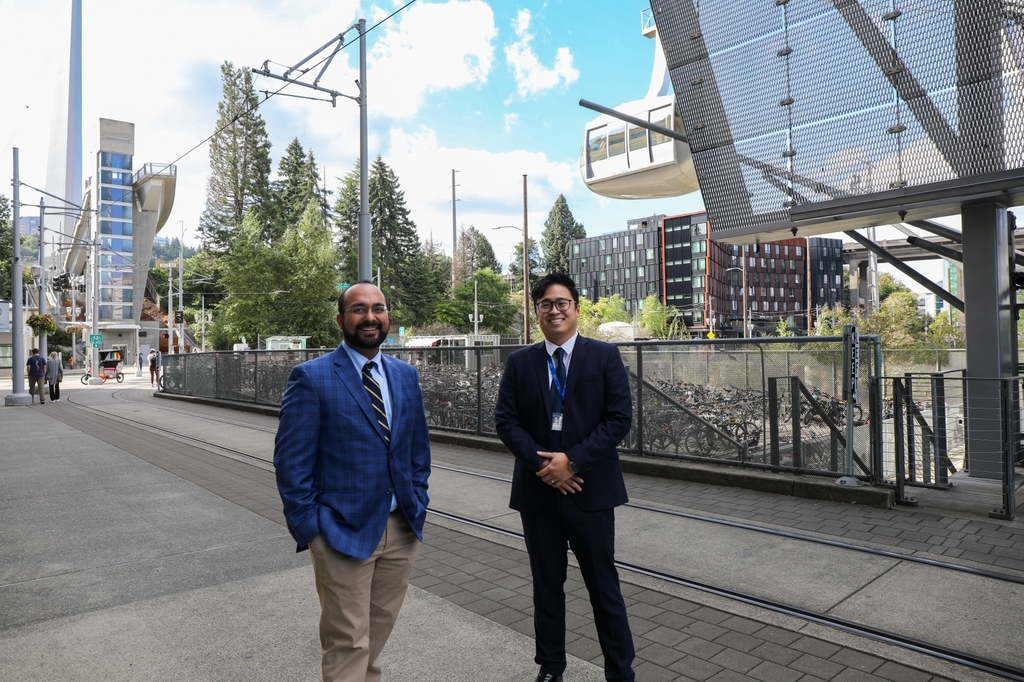 Sushant Puri, MBBS, izquierda, y Huan Vo, M.D., parados cerca del tranvía aéreo OHSU en CHH1 en Portland.